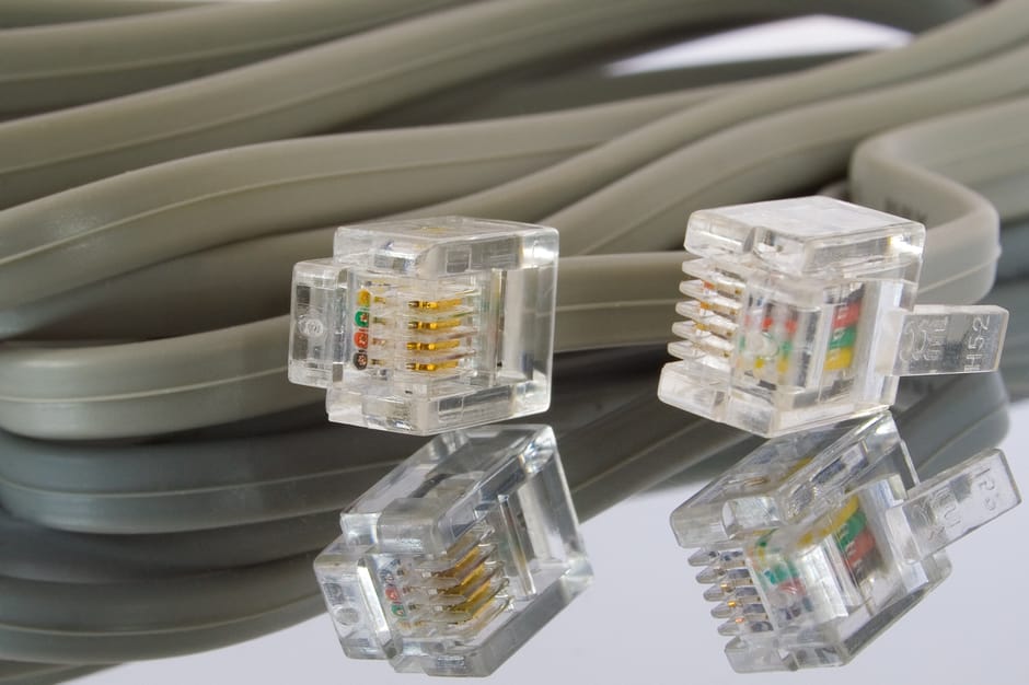 Close-up image of several grey Ethernet cables coiled together, with four transparent RJ45 connectors attached to the ends. The connectors reveal small, gold-plated pins and colored wiring inside, ind